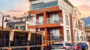 A hotel with a restaurant on the ground floor, multiple balconies, and parked cars. - Sarehotel (Kusadasi)