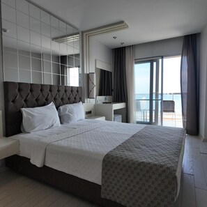 Une chambre d’hôtel moderne, dotée d’un grand lit, d’une table de chevet, d’un miroir, d’un bureau et offrant une vue sur la mer.