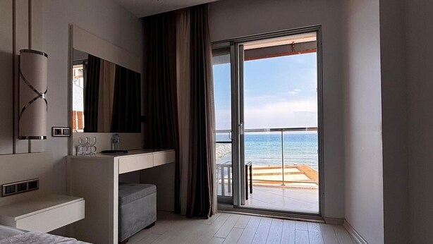 A hotel room with a bed, a desk, a TV, and a balcony with a view of the sea. - Sarehotel (Kusadasi)