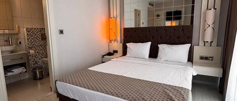 Habitación de hotel moderna con una cama grande, una mesita de noche, un espejo y un baño visible a través de una puerta abierta.