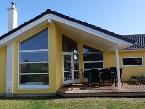 Um edifício amarelo com varanda coberta, janelas amplas e chaminé.