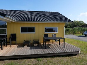 Um edifício amarelo com telhado em telhas, um alpendre com mobiliário de exterior e um carro estacionado nas proximidades.