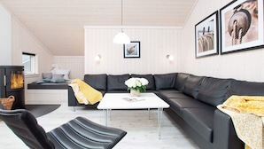 Ein modernes Wohnzimmer mit einer Eckcouch, einem schwarzen Ledersessel, einem weißen Couchtisch, einem Kamin und gerahmten Kunstwerken an den Wänden.