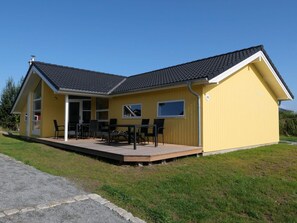 Um edifício amarelo com telhado plano, varanda coberta com móveis de exterior e o número '70' na lateral.