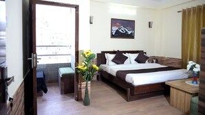 Habitación de hotel con cama, mesita de noche, un florero con flores, un cuadro en la pared y vistas a través de una puerta abierta.