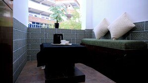 Un rincón con asientos, una mesa negra, una planta en maceta y vista a un edificio.
