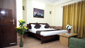 Una habitación de hotel con una cama de madera, una mesita de noche, un sillón verde, un jarrón con flores y un cuadro en la pared.