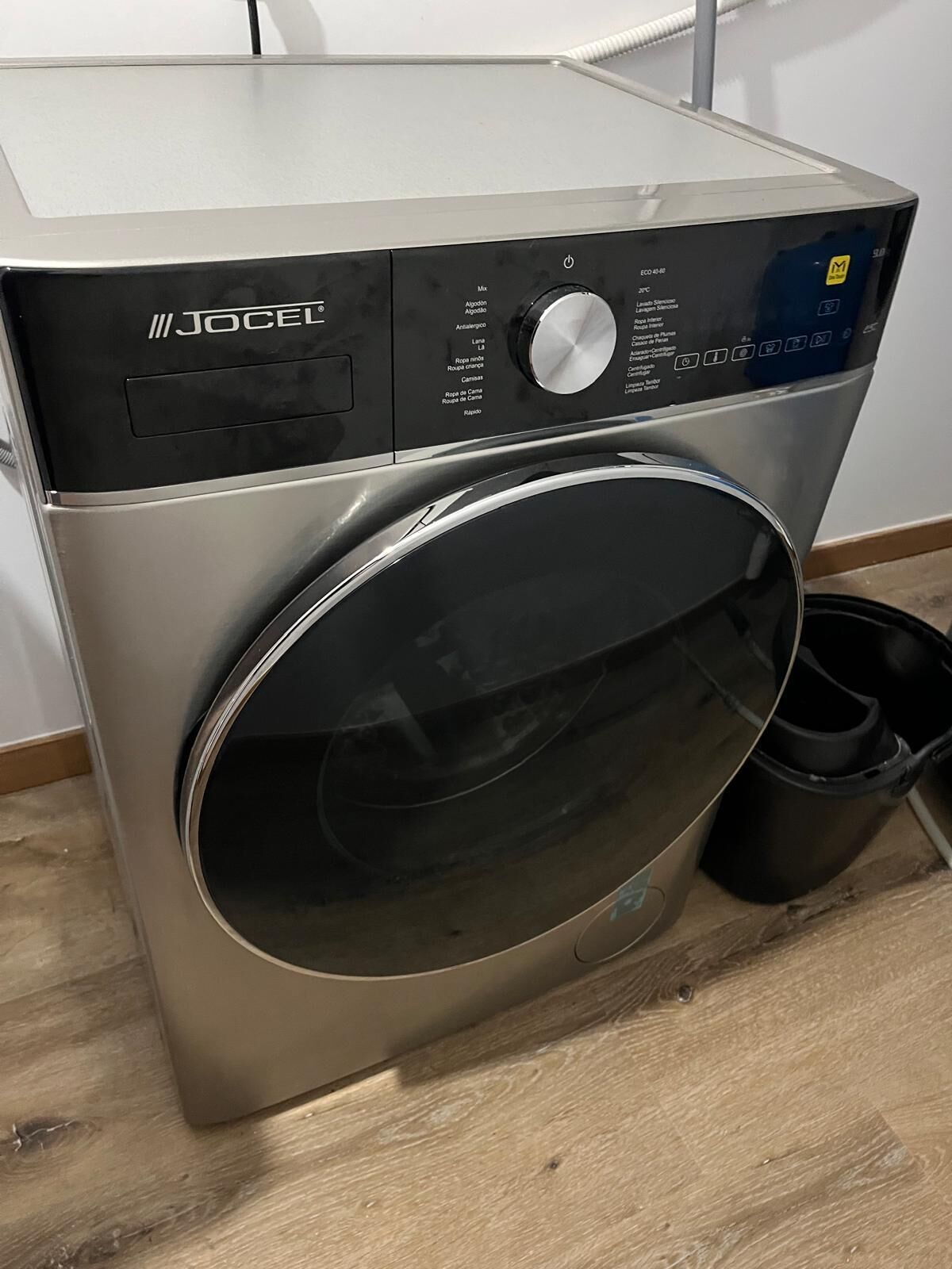 A front view of a front-loading washing machine with a control panel, a digital display, and a stainless steel door.
