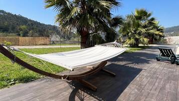 Un'amaca su un pontile di legno con vista su palme e una collina in lontananza.