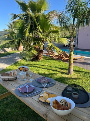 An outdoor dining setup with a table set for two, a pool, and palm trees in the background.