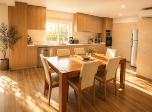 A modern kitchen with wooden cabinets, a dining table with chairs, a built-in oven, and a refrigerator.