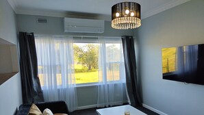 Une pièce comprenant un canapé, une table basse, un téléviseur fixé au mur et une fenêtre avec des rideaux.