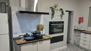 Une cuisine moderne équipée d’un four encastré, d’un four à micro-ondes et d’une cuisinière à gaz. On y trouve des placards, une planche à découper et une plante accrochée au mur.