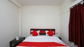 Una habitación de hotel con cama, mesita de noche, cortina roja y un equipo de aire acondicionado.