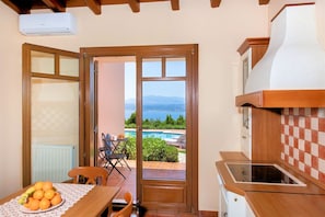 A kitchen with a view of a swimming pool and mountains, a dining area with a table and chairs, and a ceiling fan. - Villa Marathe Lux | Akrotiri, Chania | Sea Views | Private Pool (Crete)