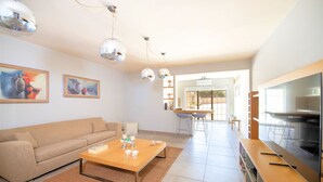 Un soggiorno moderno con divano, tavolino e TV. Alle pareti sono presenti dipinti e, sullo sfondo, una zona pranzo.