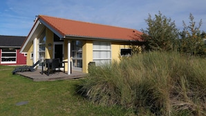 A small yellow building with a red roof, a patio with a table and chairs, and a number '147' on the door. - Cosy Coastal Stay for 6 Guests (Grossenbrode)