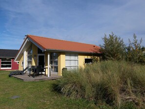 A small yellow building with a red roof, a patio with a table and chairs, and a number '147' on the door. - Cosy Coastal Stay for 6 Guests (Grossenbrode)