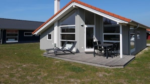 Ein modernes Haus mit Terrasse, großen Fenstern und Schornstein.