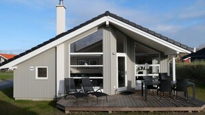 A modern, single-story building with a sloped roof, a deck with outdoor seating, and a visible chimney. - 4 Star Holiday Home in Grossenbrode (Grossenbrode)