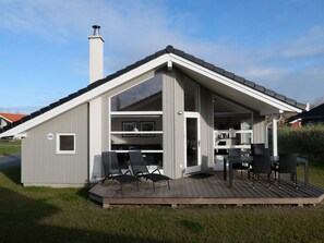 A modern, single-story building with a sloped roof, a deck with outdoor seating, and a visible chimney. - 4 Star Holiday Home in Grossenbrode (Grossenbrode)