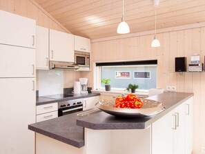 A modern kitchen with wooden cabinets, a microwave, stove, and a large island with a bowl of tomatoes. - 4 Star Holiday Home in Grossenbrode (Grossenbrode)