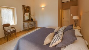 Et soveværelse med seng, kommode, stol, spejl og natbord med lampe.