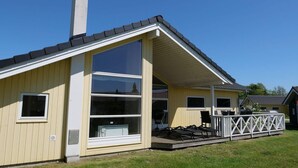 Yhden kerroksen talo, jossa on suuri ikkuna, savupiippu ja terassi, jossa on tuoleja.