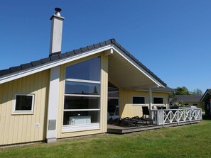 A single-story building with a large window, a chimney, and a deck with chairs. - 4 Star Holiday Home in Grossenbrode (Grossenbrode)