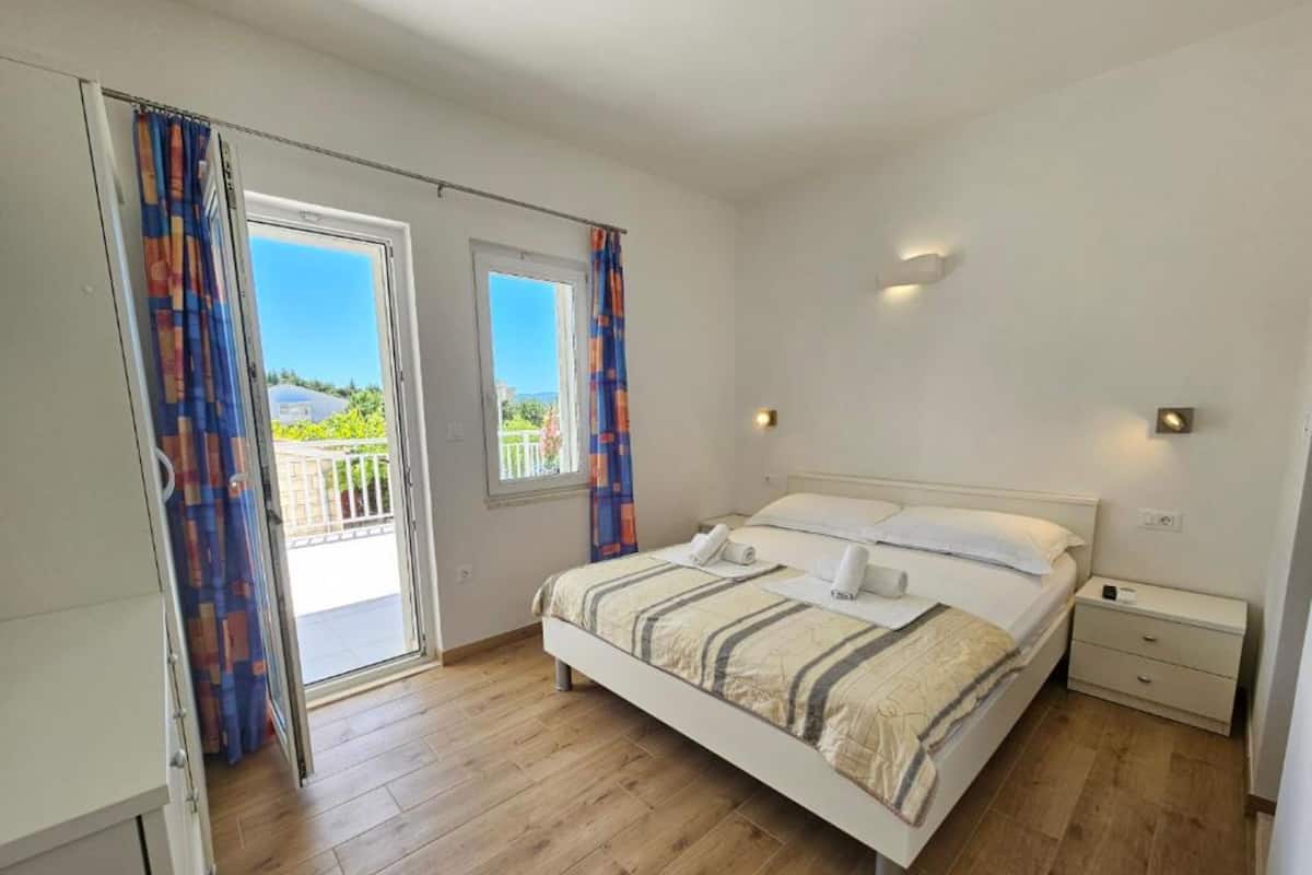 A bedroom with a bed, two bedside tables, a window, and a door leading to a balcony.