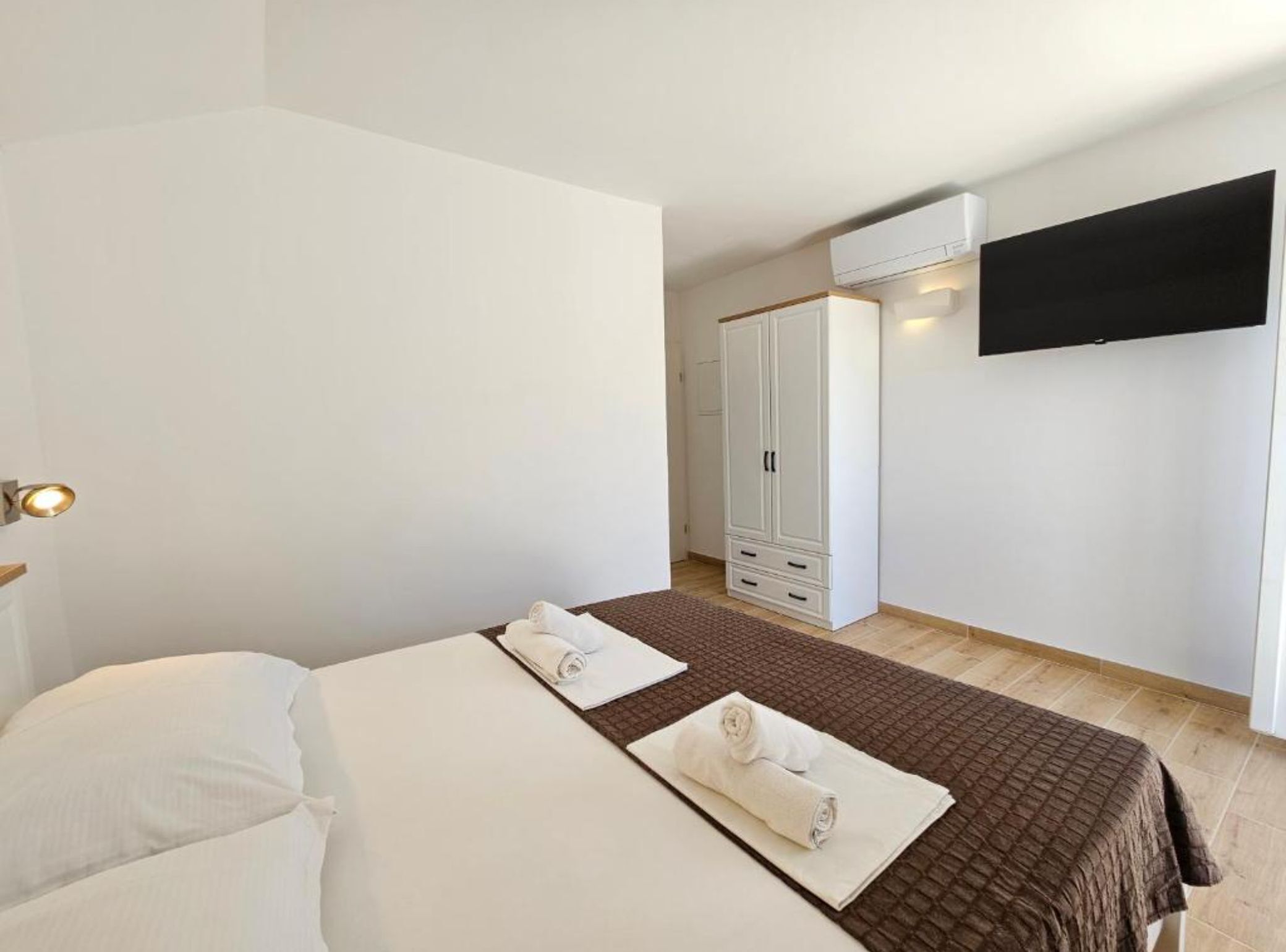 A bedroom with a bed, a wardrobe, a flat-screen TV mounted on the wall, and a window.
