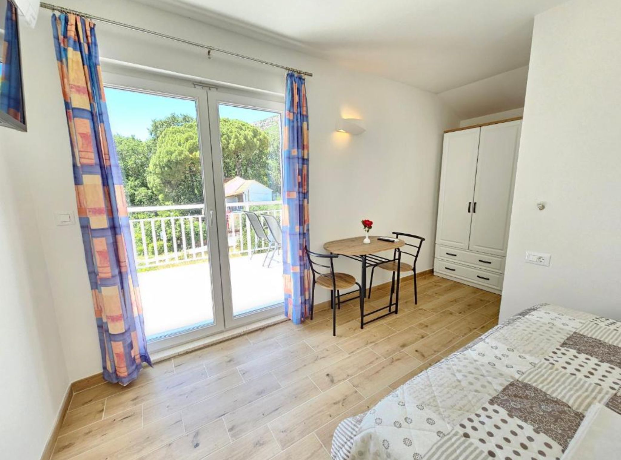Un dormitorio con cama, una mesita con sillas, un balcón con vistas y un armario.