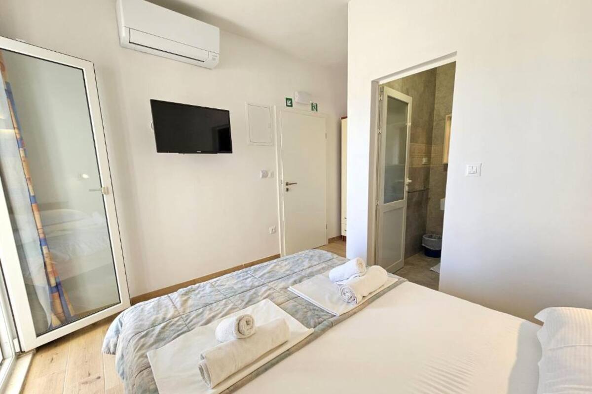 A hotel room with a bed, a TV, a shower, and a door leading to a bathroom.