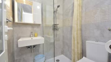 Et badeværelse med en glas brusekabine, en hvid vask, et toilet og en blå skraldespand.
