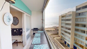 A balcony with a view of the beach, a table, chairs, and a clock on the wall. - Grande Maree - Apartment Sea View, 100m from the beach (Saint-Hilaire-de-Riez)