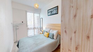 A bedroom with a bed, a bedside lamp, a window with curtains, and a framed picture on the wall. - Grande Maree - Apartment Sea View, 100m from the beach (Saint-Hilaire-de-Riez)