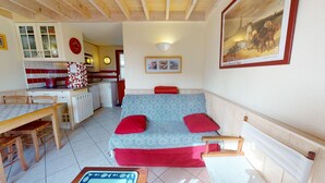 Une pièce confortable avec une kitchenette, un coin repas et un canapé agrémenté de coussins rouges.