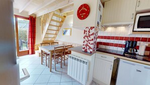 Une cuisine avec une table en bois, des chaises, un crédence carrelée en rouge et blanc, une horloge et un four à micro-ondes.