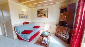 A room with a bed, a small table, a cabinet, and a framed picture on the wall.
