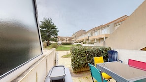 A balcony with a table, chairs, and a view of a courtyard with buildings in the background. - Jardin Marin - Pool & Terrace, Beach 250 meters away (Saint-Hilaire-de-Riez)