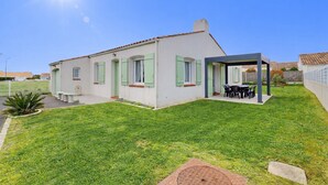 Een gelijkvloers huis met een overdekte patio, een kleine tuin en een heldere lucht.
