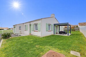 A single-story house with a covered patio, a small garden, and a clear sky. - Parenthese du Patis - House for 6 + enclosed garden (Saint-Hilaire-de-Riez)
