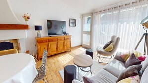Ein Wohnzimmer mit Fernseher, Holzschrank, Sofa und Esstisch.