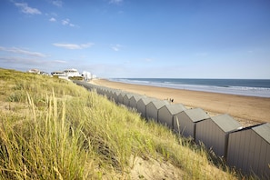 A beach with a row of beach huts, a sandy shore, and a grassy dune area. - High tide at Les Demoiselles—beach 300 meters away (Saint-Hilaire-de-Riez)