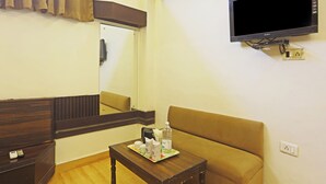 A hotel room with a brown sofa, a small table with a tray of items, a mounted TV, and an air conditioning unit. - Hotel Hilife (New Delhi)