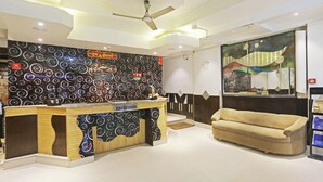 A reception area with a counter, a ceiling fan, a sofa, and a wall with a circular pattern. - Hotel Hilife (New Delhi)