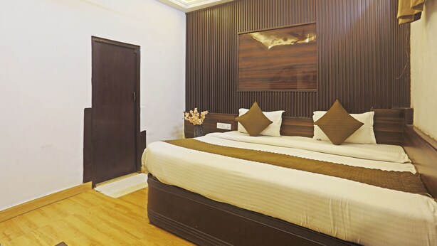 A bedroom with a large bed, a wooden headboard, a wall-mounted artwork, and a door. - Hotel Hilife (New Delhi)