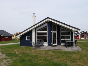 Ein modernes Haus mit einem großen Glasbalkon, einem Schornstein und einer Terrasse mit Sitzgelegenheiten.