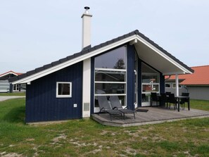A modern house with a large glass window, a chimney, and a deck with chairs. - 4 Star Holiday Home in Grossenbrode (Grossenbrode)