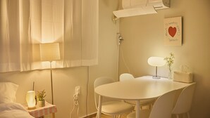 Ein Hotelzimmer mit einem Bett, einem Nachttisch mit Lampe, einer kleinen Topfpflanze, einem runden Tisch mit Stühlen und einer Wand-Klimaanlage.